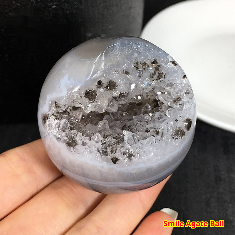 Hand holding a smile agate crystal ball for altar with sparkling crystal clusters inside