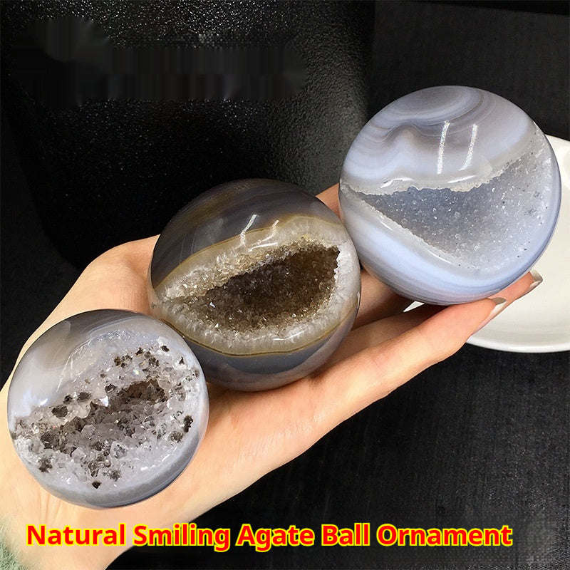 Hand holding natural smiling agate crystal ball for altar with visible crystal formations