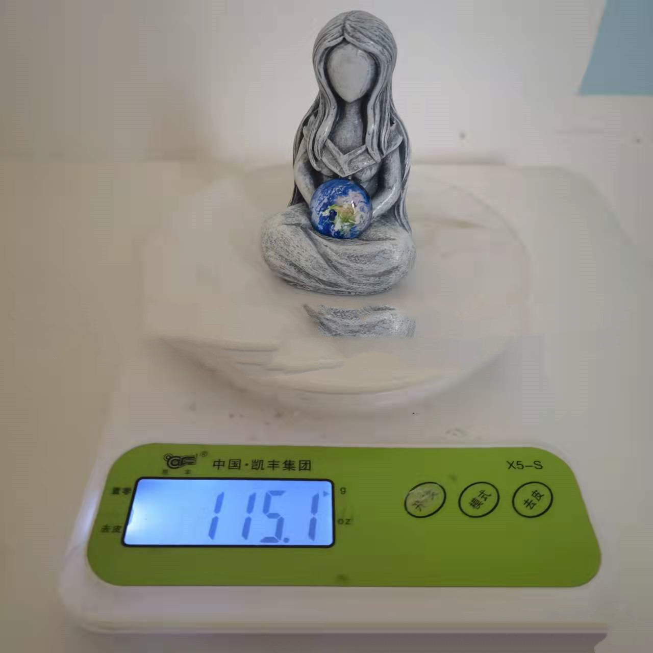 Sacred Moon Candle Co earth goddess Figurine seated holding a small blue earth globe on a dish on a digital scale reading 115.1 g