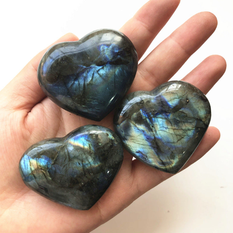 Three polished labradorite heart crystal stones with blue flash held in a hand by Sacred Moon Candle Co