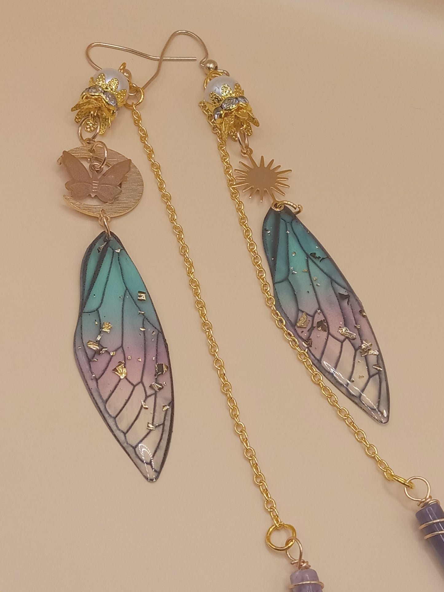 Sacred Moon Candle Co blue and violet fairy earrings with gold chains, sun and butterfly charms, stained glass wings