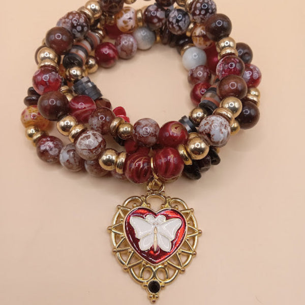 Sacred Moon Candle Co moth and flame bracelet stack featuring red and brown beads with gold accents and butterfly heart charm