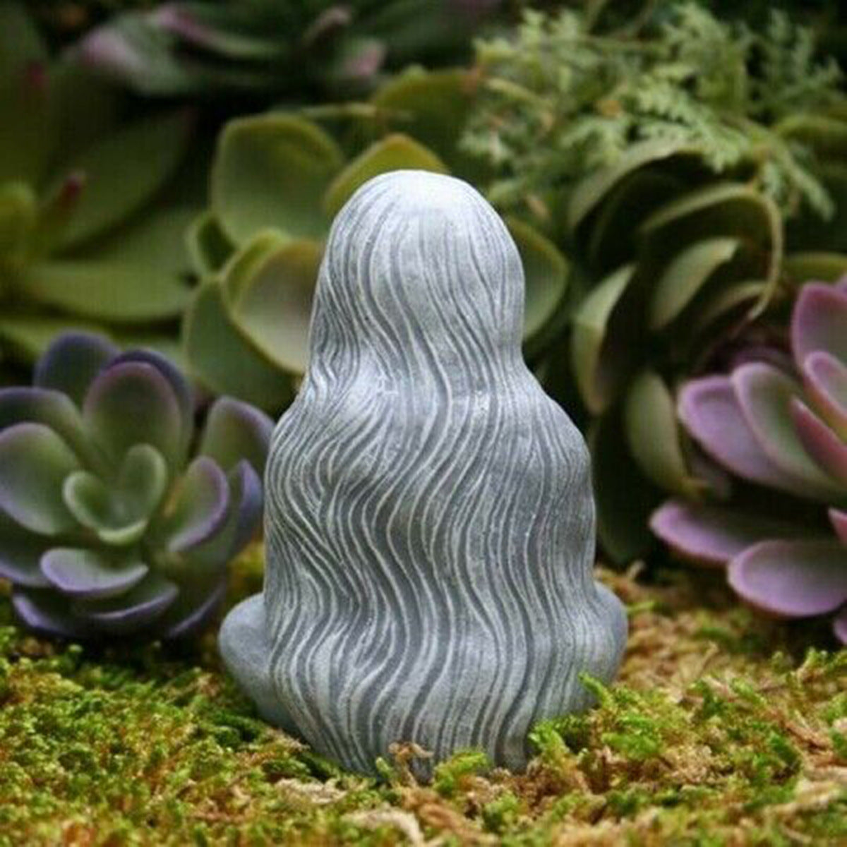 Grey stone moon goddess alter figurine seated with flowing hair on moss and succulents