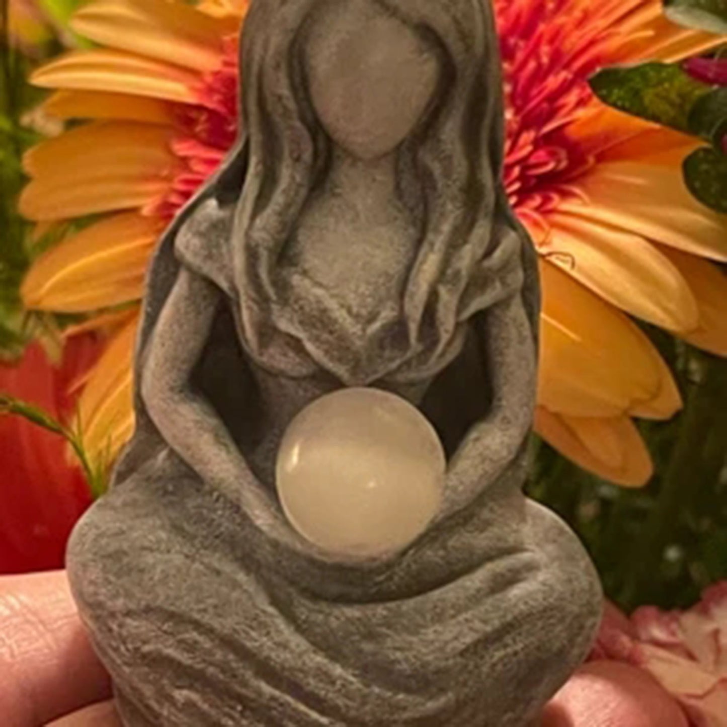 Sacred Moon Candle Co gray seated moon goddess alter figurine . holding a milky selenite orb amid floral background