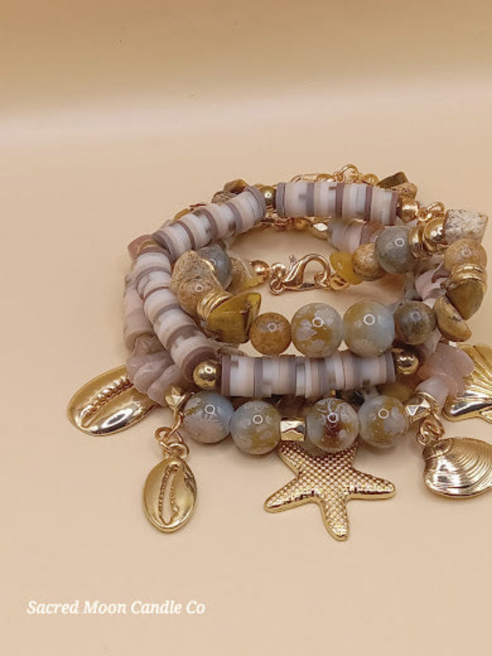 Bohemian natural stone bracelet stack with gold charms by Sacred Moon Candle Co on beige background