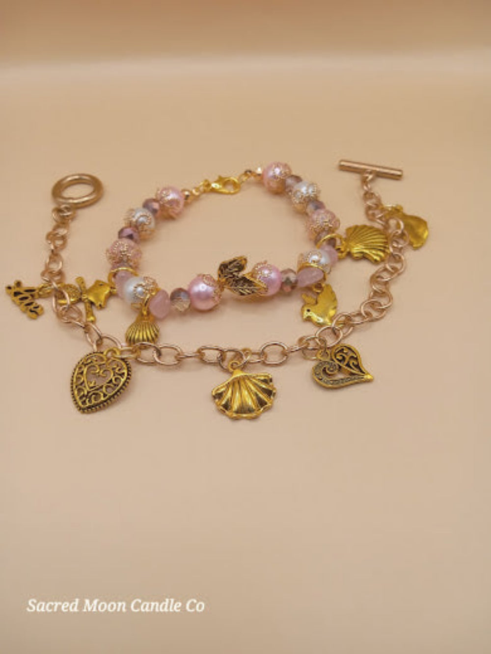 Aphrodite bracelet set by Sacred Moon Candle Co featuring gold charms and pink beaded bracelet stack