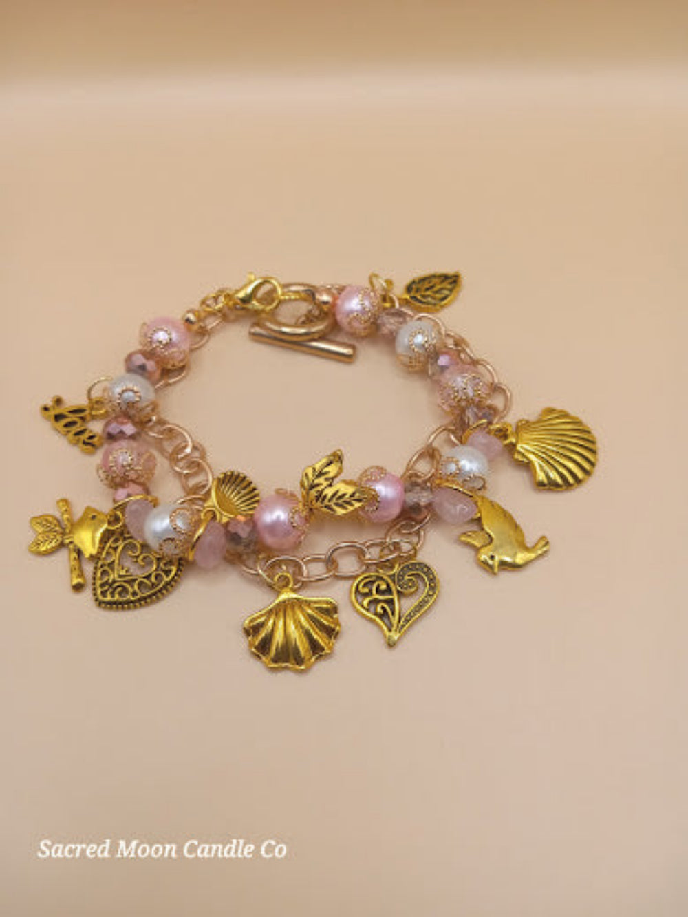 Aphrodite bracelet set by Sacred Moon Candle Co featuring gold charms and pink and white beads in a bracelet stack