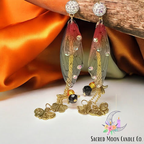 Delicate firefly fairy earrings with translucent wings, gold chains, black beads, and decorative gold charms