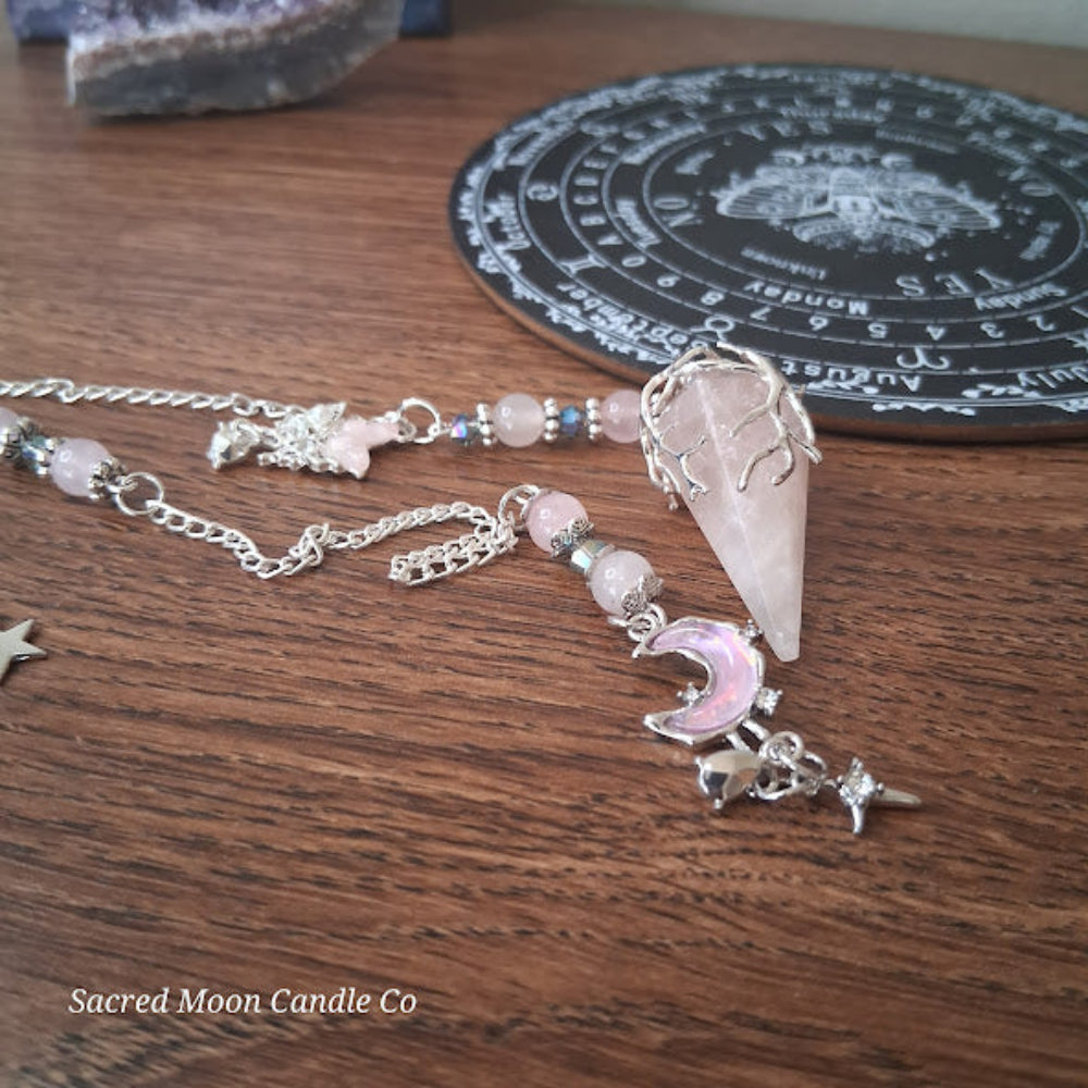 Rose quartz pendulum for divination with silver chain and celestial charms on wooden surface