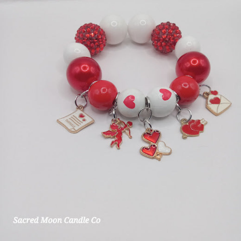 Cupid themed bubblegum beaded bracelet with red and white beads and love-themed charms by Sacred Moon Candle Co