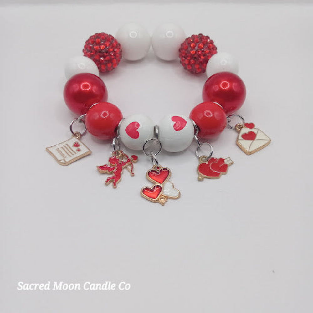 Cupid themed bubblegum beaded bracelet with red and white beads and love-themed charms from Sacred Moon Candle Co