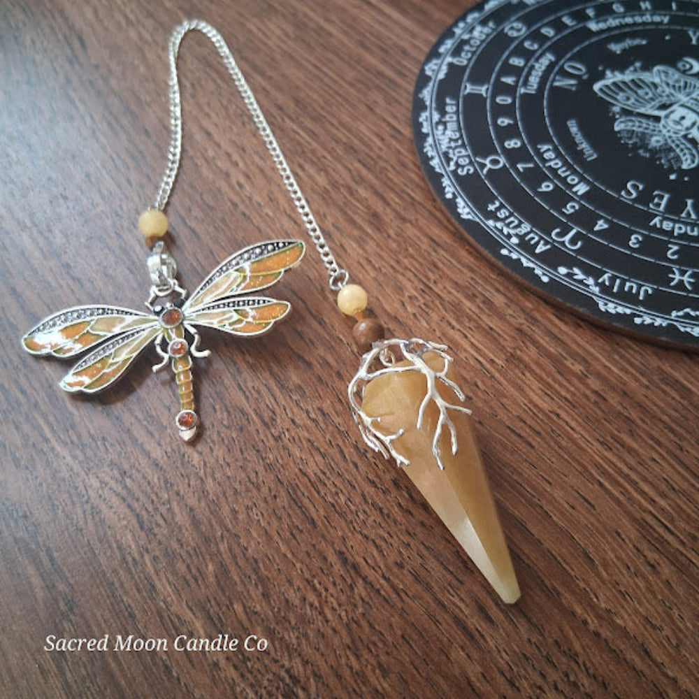 Golden healer quartz pendulum with silver dragonfly charm and wooden beads on wooden surface