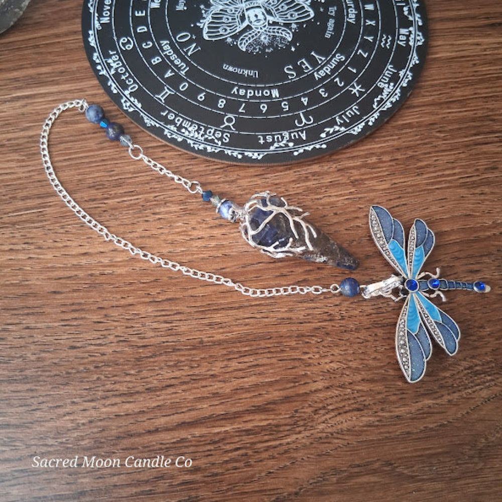 Sacred Moon Candle Co altar tool featuring a sodalite and lapis lazuli pendulum with a dragonfly charm on wood