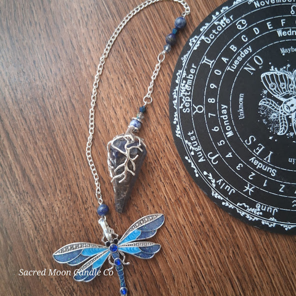 Sodalite and lapis lazuli pendulum with dragonfly charm on wooden surface beside black calendar board