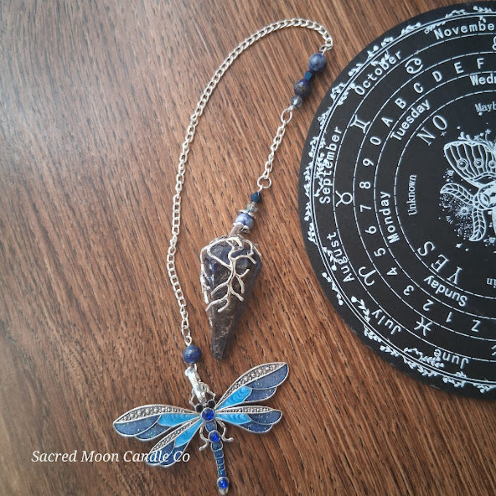 Sodalite and lapis lazuli pendulum with dragonfly charm on wooden surface by Sacred Moon Candle Co