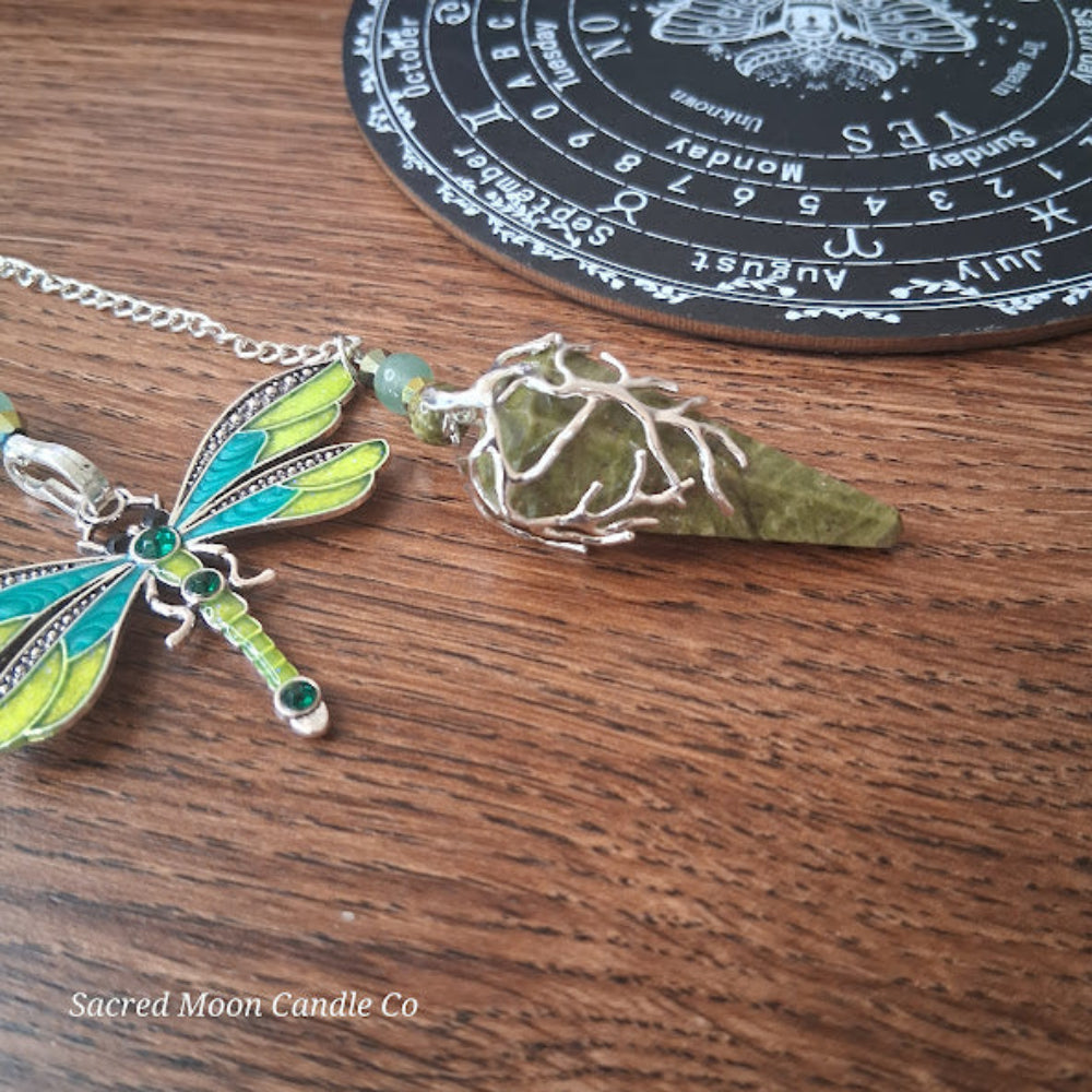 Unakite amazonite dragonfly pendulum with green and blue wings on wooden surface and black divination board