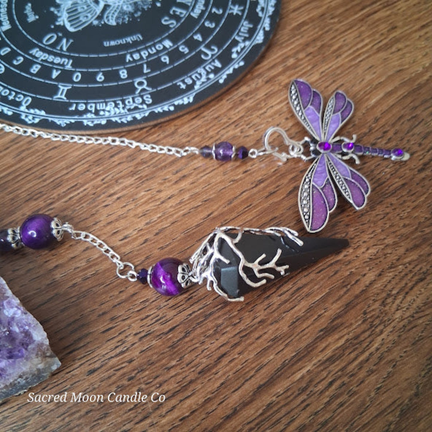 black tourmaline Purple Tigers Eye Dragonfly Pendulum altar tool by Sacred Moon Candle Co on wooden surface