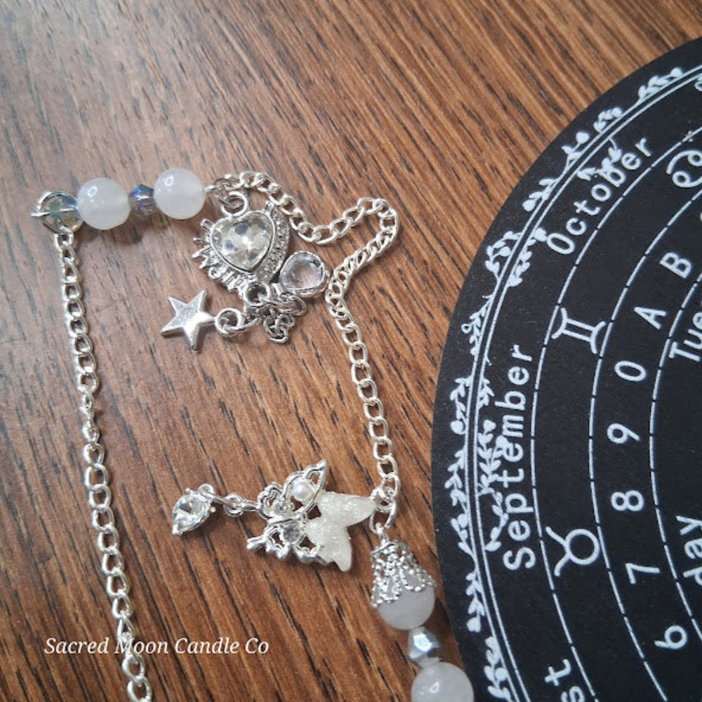 Sacred Moon Candle Co selenite moon pendulum with silver chain and crystal charms on wooden surface