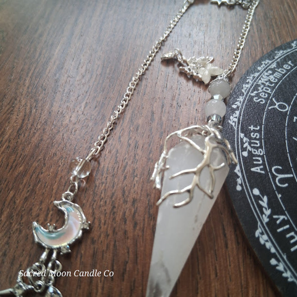 Selenite moon pendulum with silver chain and crescent moon charm from Sacred Moon Candle Co on wooden surface