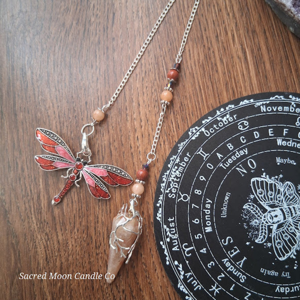 Sunstone dragonfly pendulum for divination with silver chain and beads next to a black divination board