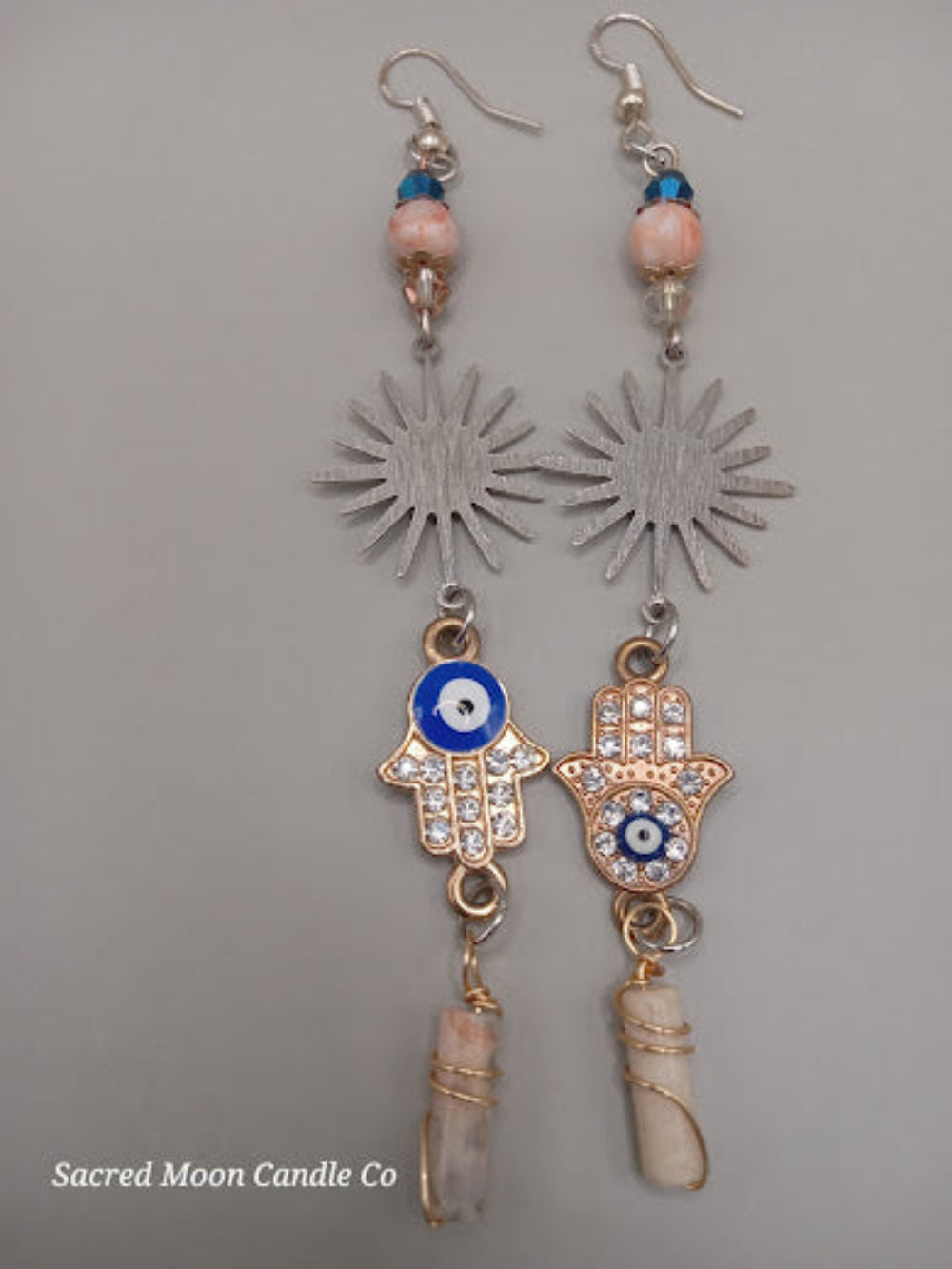 Sunburst Hamsa evil eye earrings featuring silver sunburst, blue evil eye charms, and wrapped crystal drops