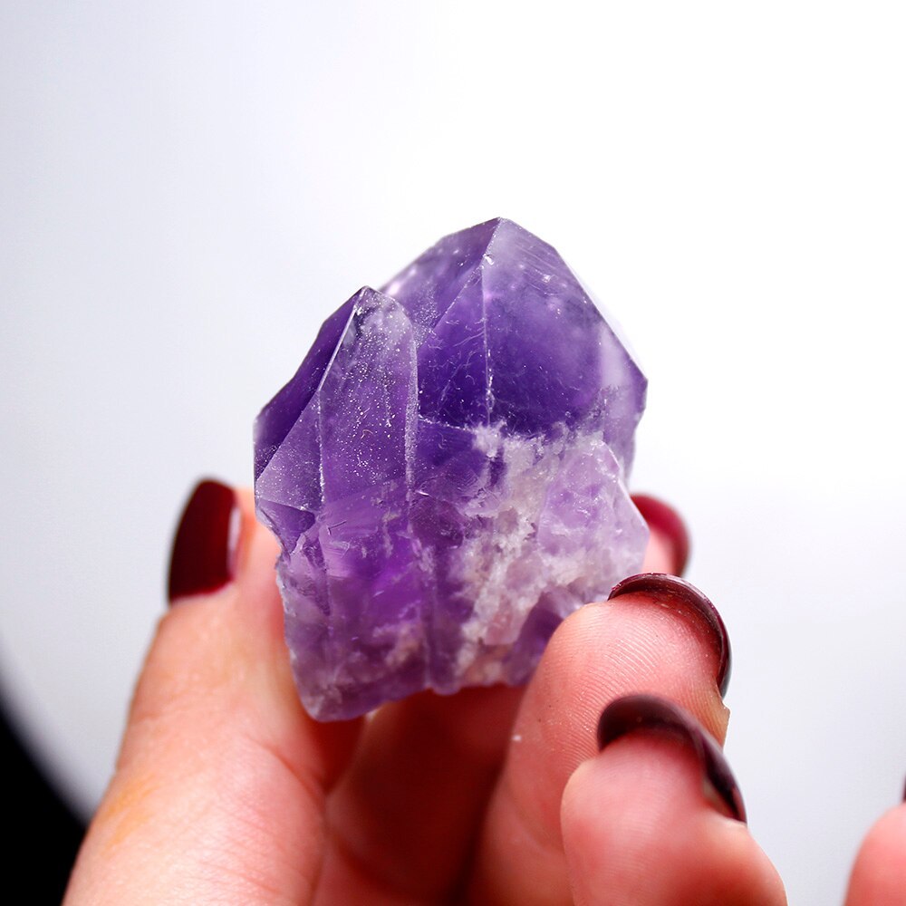 Hand holding a natural amethyst crystal points natural with purple hues by Sacred Moon Candle Co