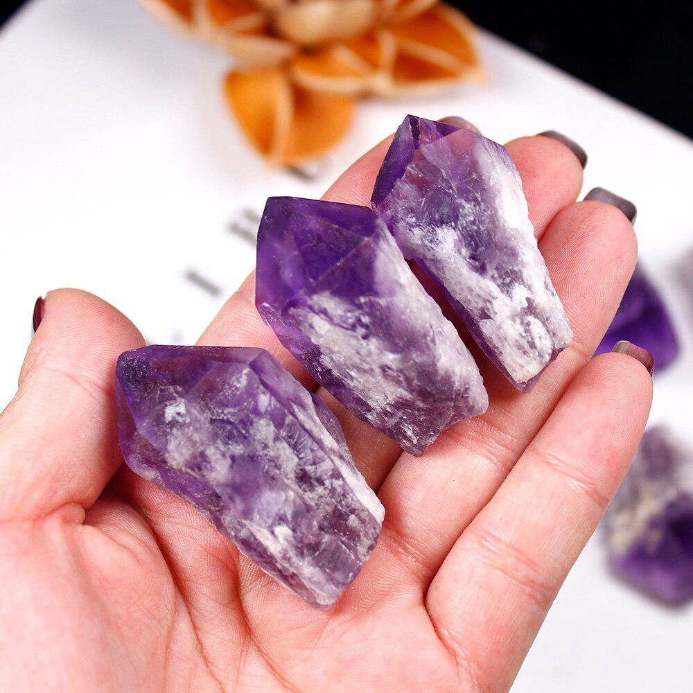 Hand holding three natural amethyst crystal points with purple and white patterns