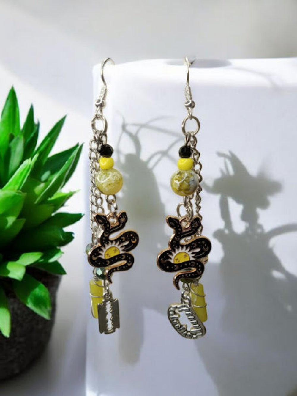 Sacred Moon Candle Co snake charm earrings with black and yellow beads and dangling silver chains