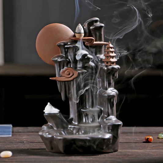 Black backflow incense burner by Sacred Moon Candle Co with intricate mountain and pagoda design emitting smoke