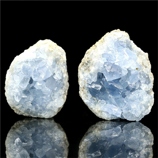 Two pale blue celestite kyanite crystal stone geode halves on black reflective surface for healing display