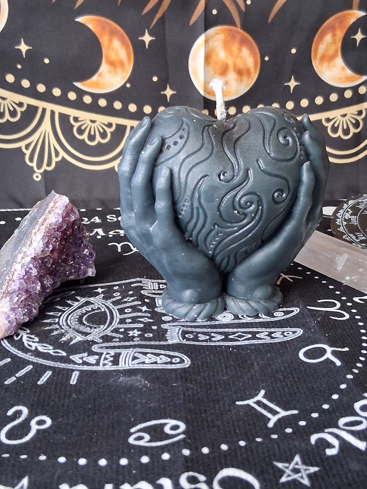 Heart in hands candle by Sacred Moon Candle Co with intricate swirl design on black decorative cloth