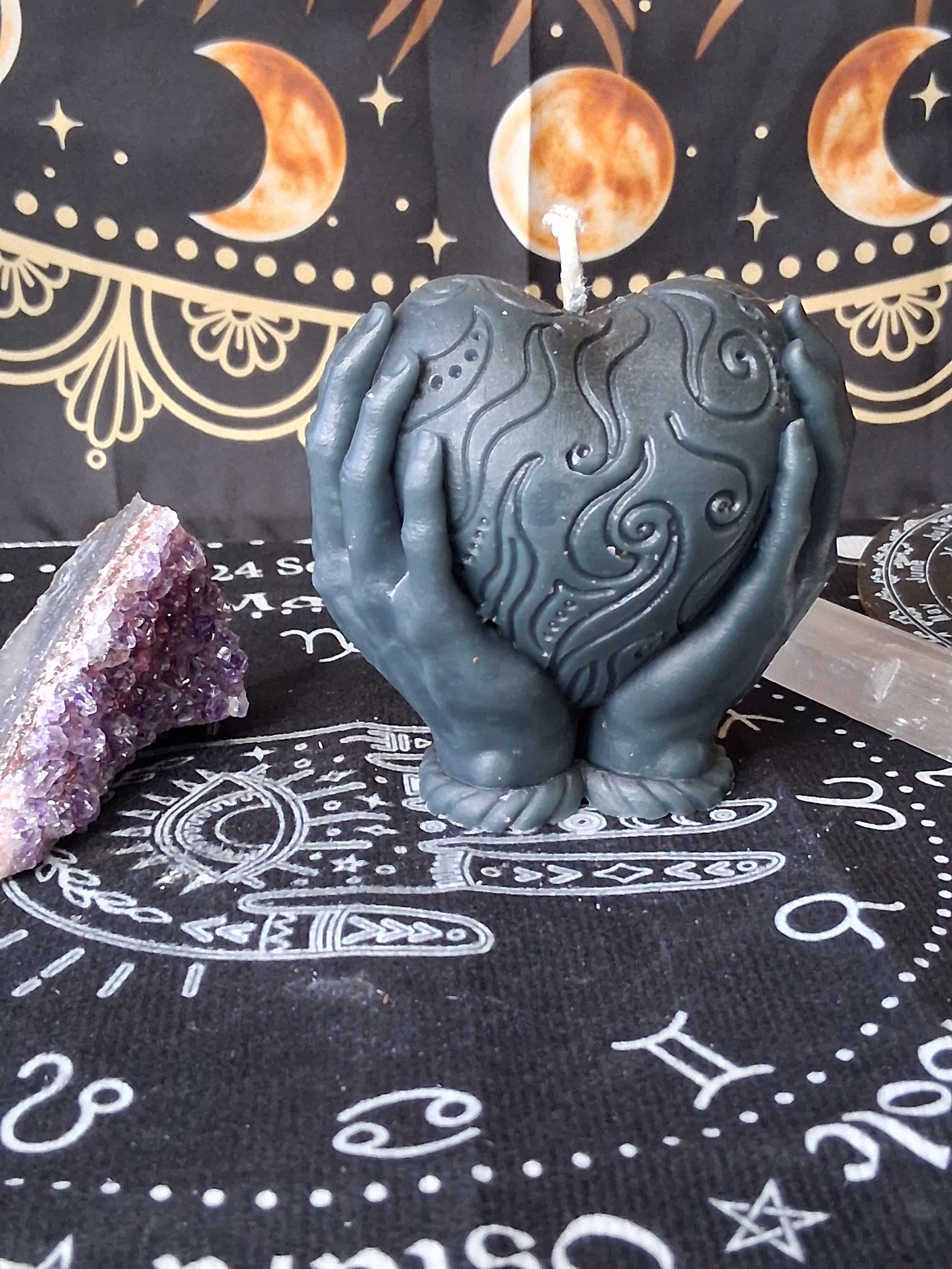 Heart in hands candle by Sacred Moon Candle Co with intricate swirl design on black decorative cloth