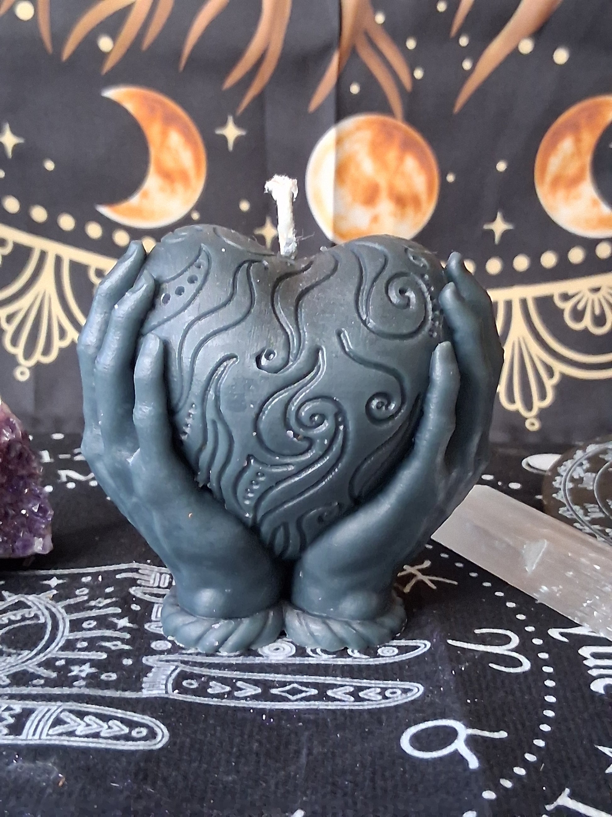 Heart in hands candle by Sacred Moon Candle Co with intricate swirl designs in dark color