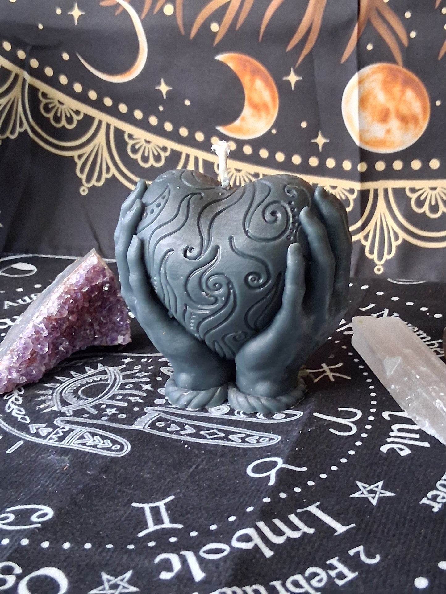 Black heart in hands candle with intricate swirl designs by Sacred Moon Candle Co on celestial cloth