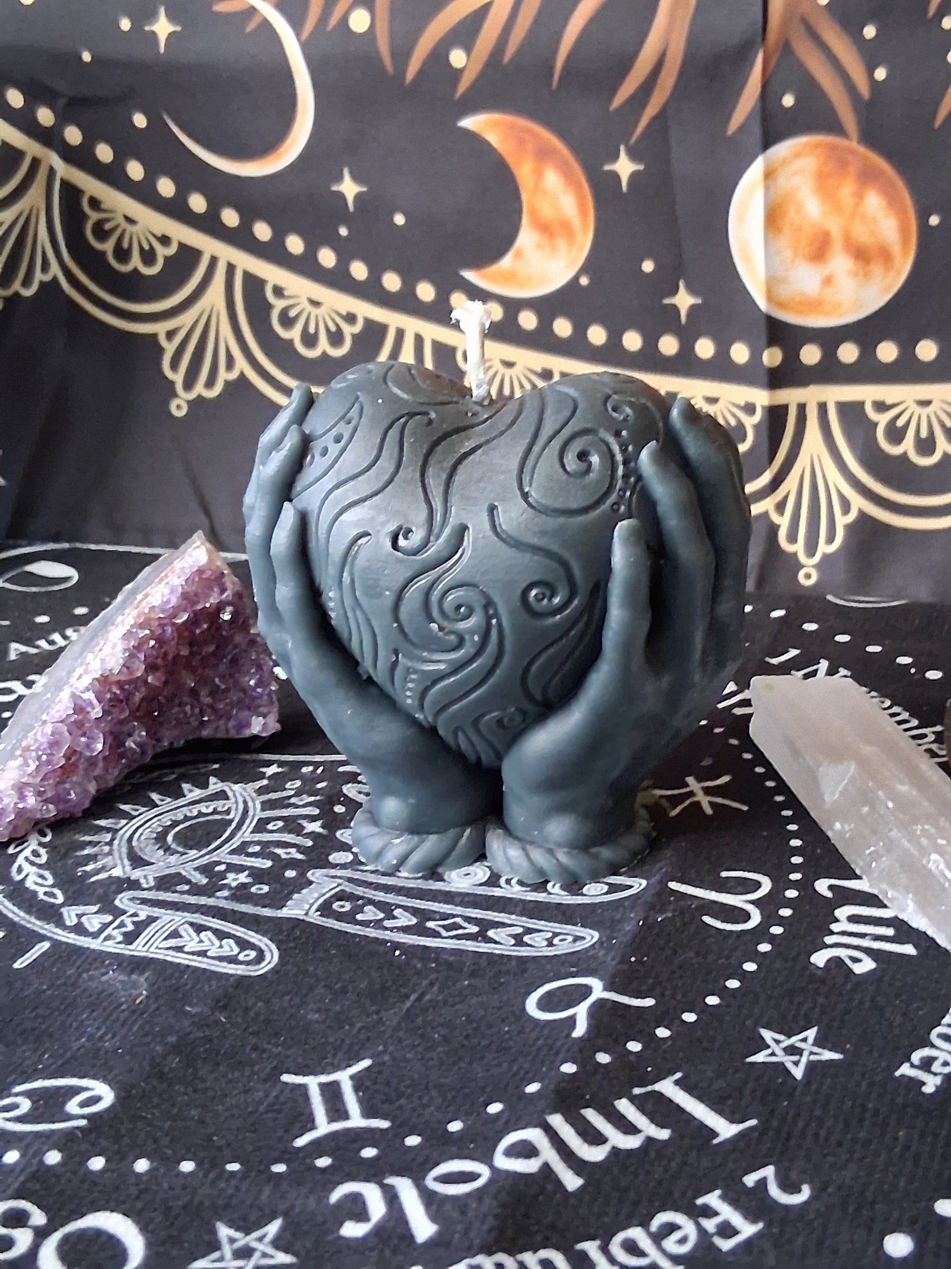 Black heart in hands candle with intricate swirl designs by Sacred Moon Candle Co on celestial cloth