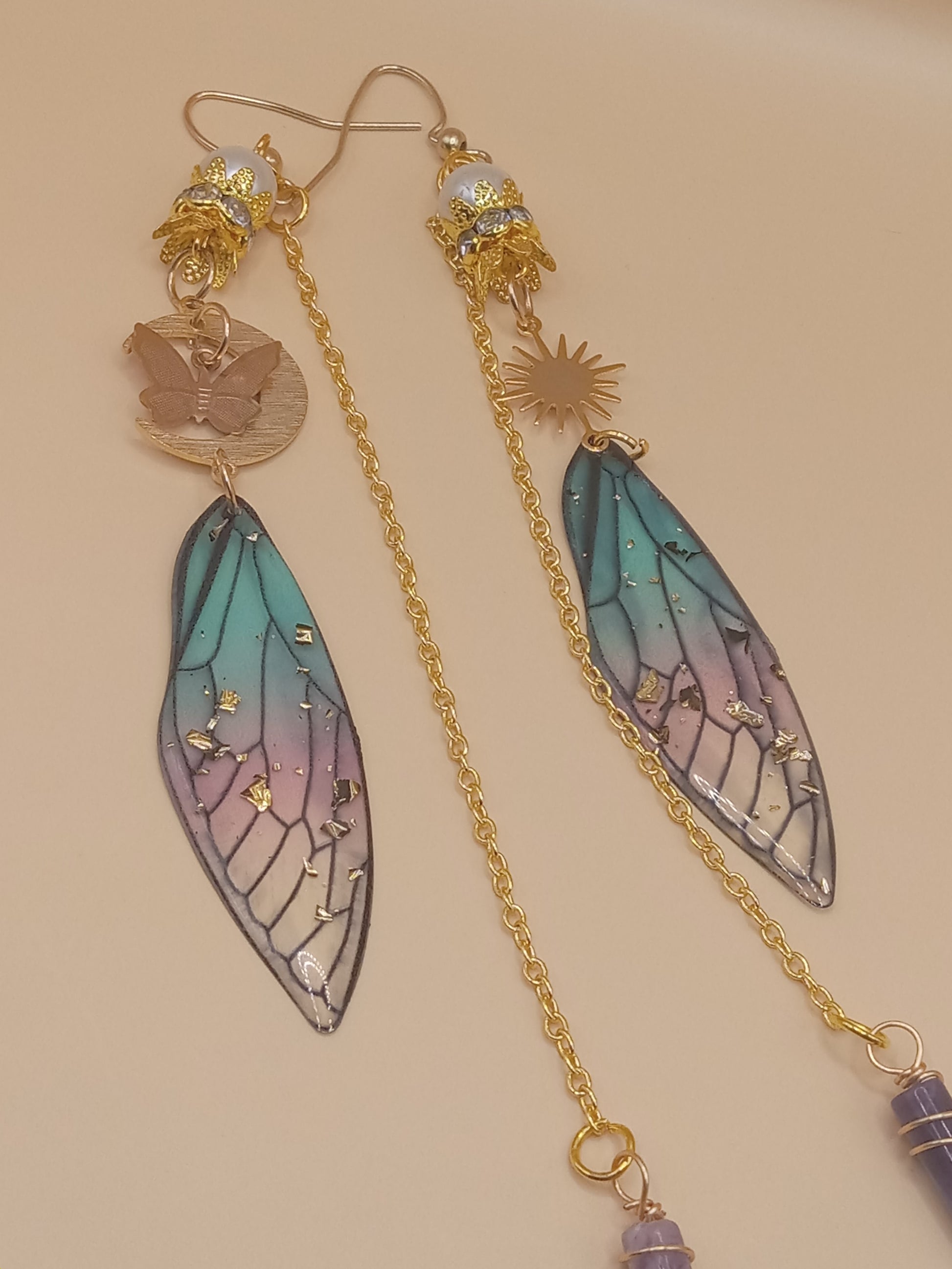 Sacred Moon Candle Co blue and violet fairy earrings with gold chains, sun and butterfly charms, stained glass wings