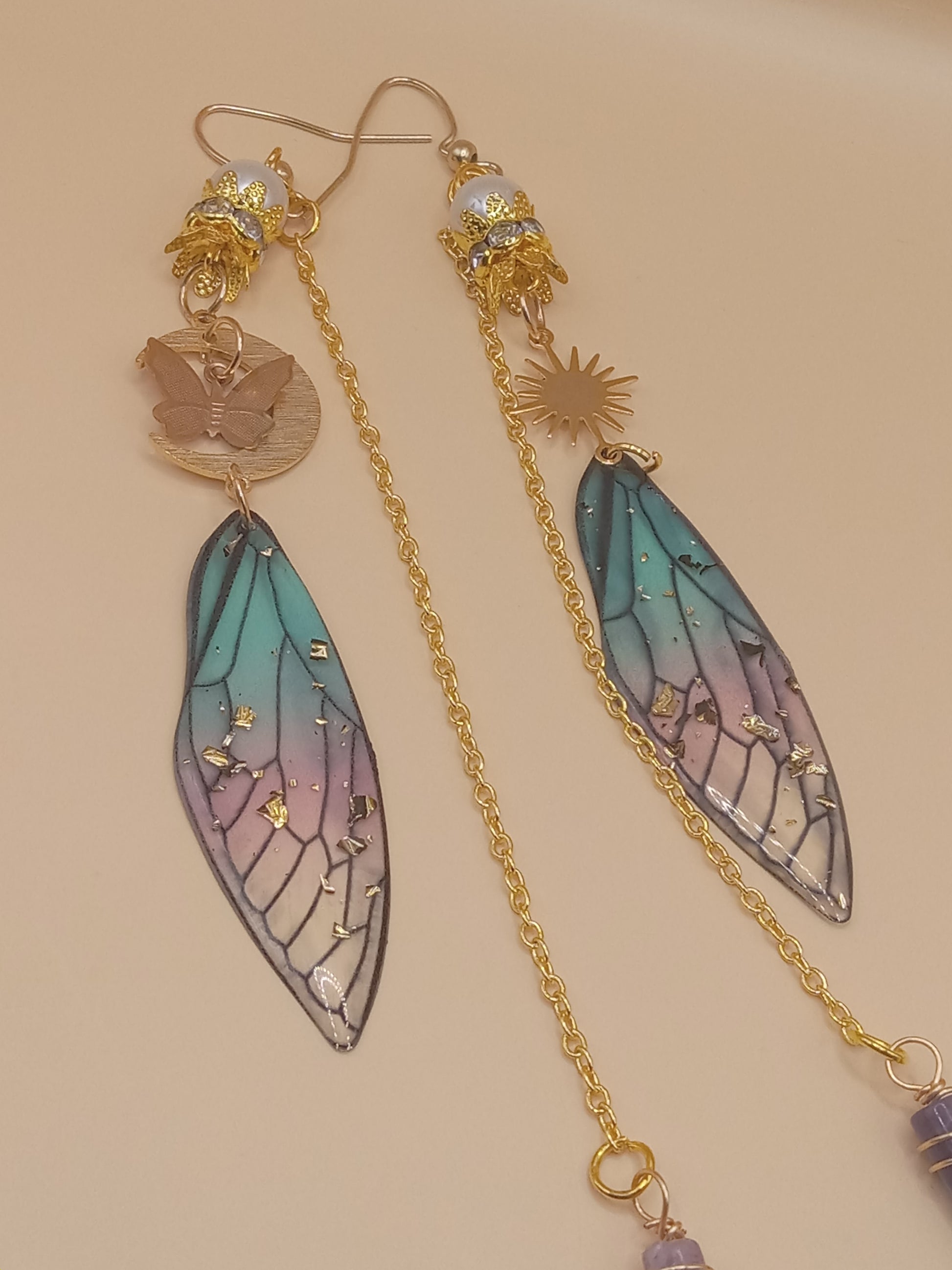 Sacred Moon Candle Co blue and violet fairy earrings with gold chain sun and butterfly charms and resin wing drops