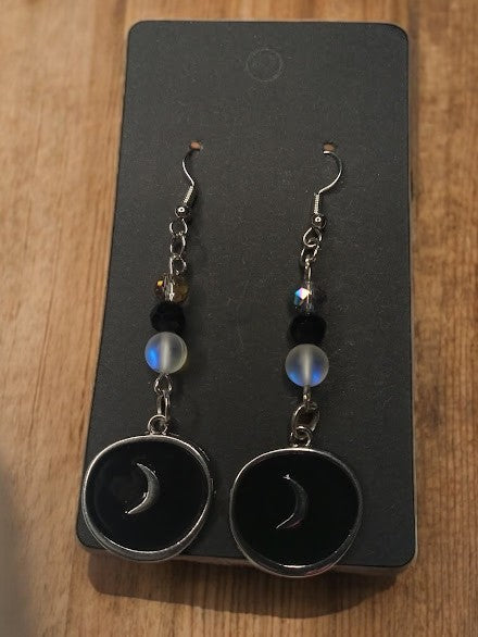 Sacred Moon Candle Co moon medallion earrings with crescent design and black beads on display card