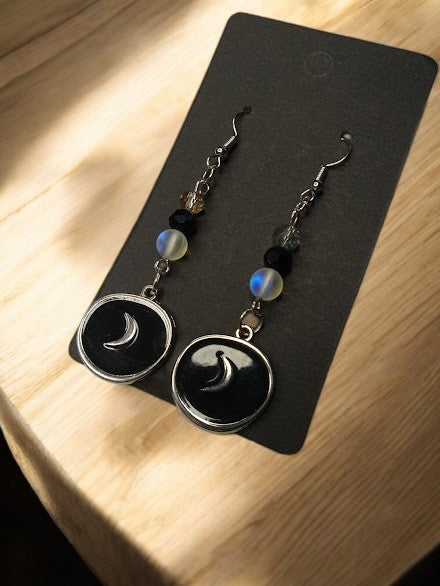 Sacred Moon Candle Co black moon medallion earrings with chain and beads on a display card