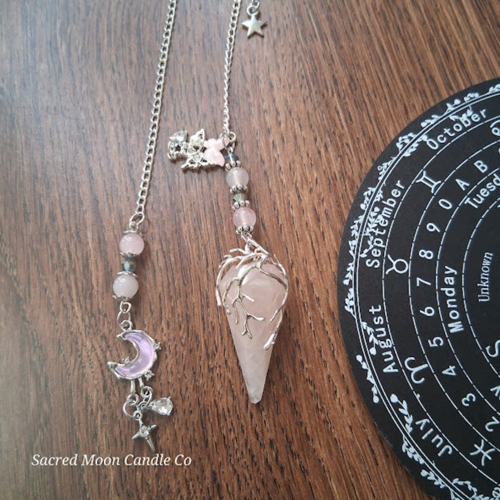 Rose quartz pendulum for divination with silver chain and crescent moon charm on wooden surface