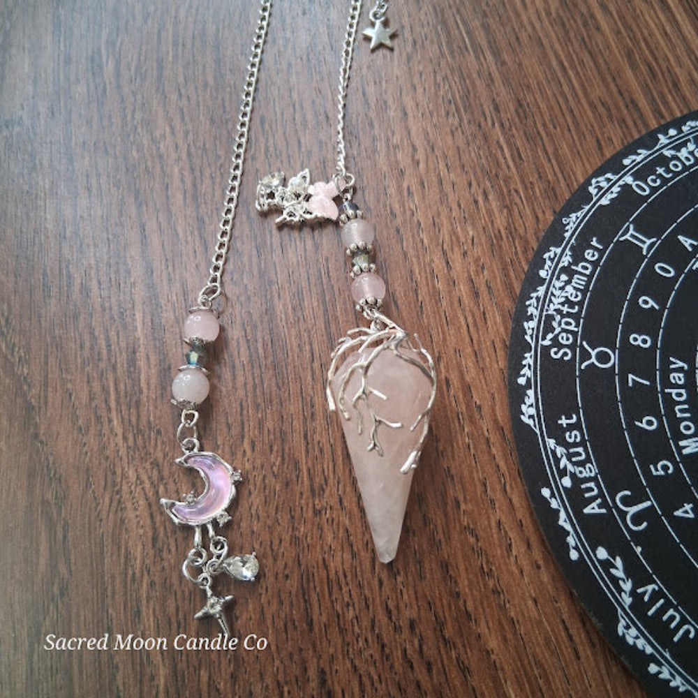 Rose quartz pendulum for divination with silver chain and crystal charms on wooden surface