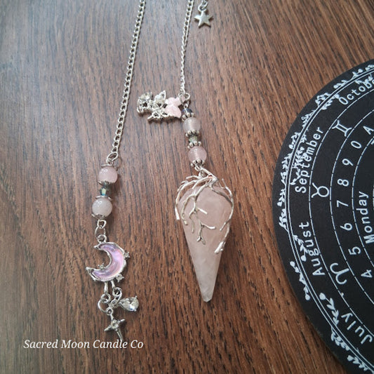 Rose quartz pendulum for divination with silver chain and crystal charms on wooden surface