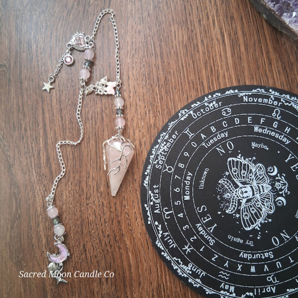 Rose quartz pendulum for divination with silver chain and charms on wooden table near divination board
