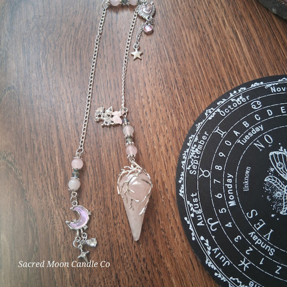 Rose quartz pendulum for divination with silver chain and charms on wooden table next to divination board