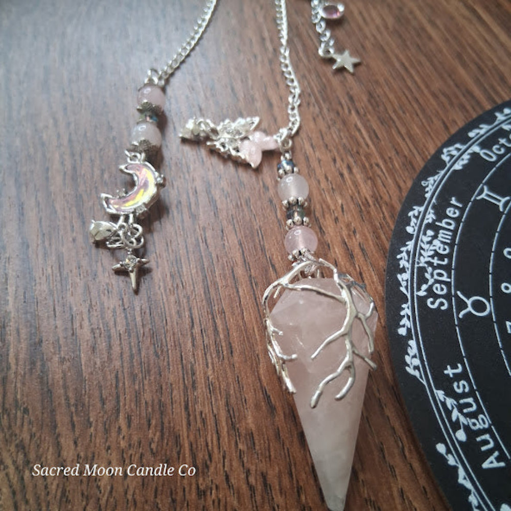 Sacred Moon Candle Co rose quartz pendulum for divination with silver chain and tree branch design on wood background