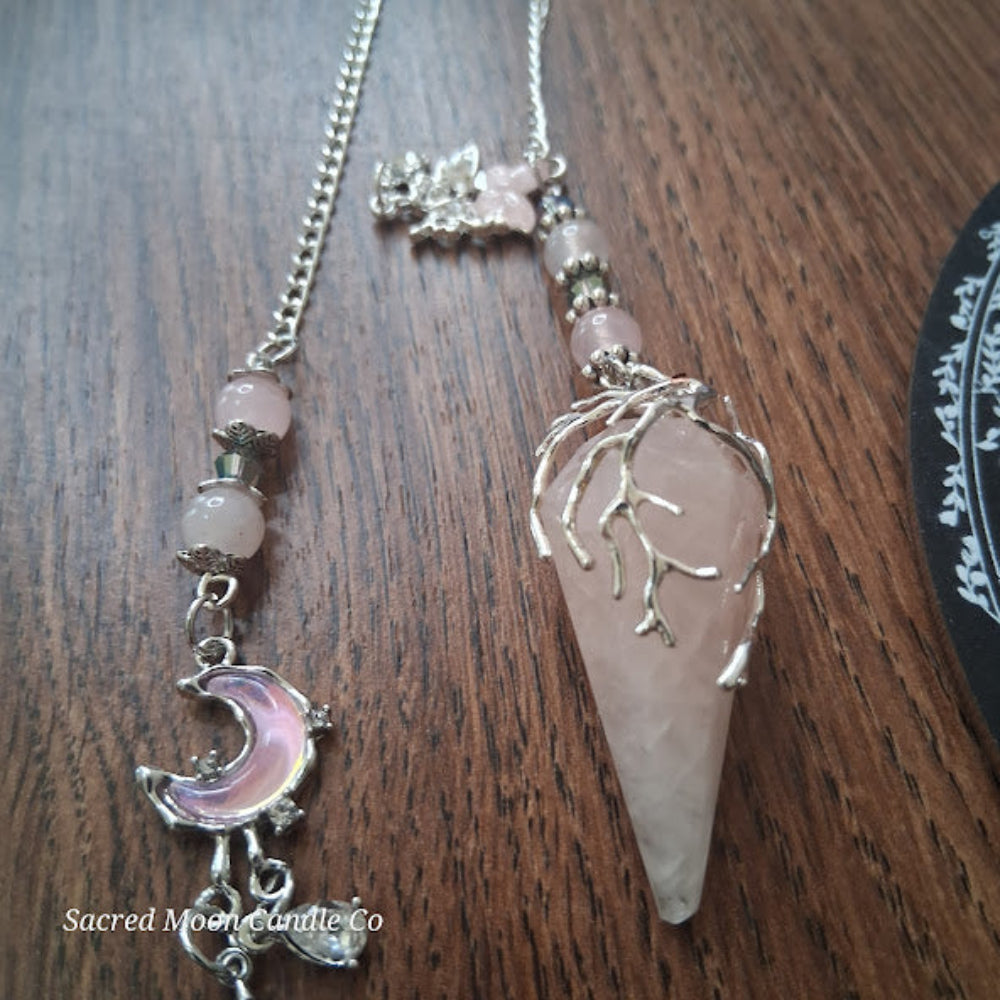 Sacred Moon Candle Co Seraphina's Heart Rose Quartz pendulum with a silver crescent moon charm and chain on wooden surface