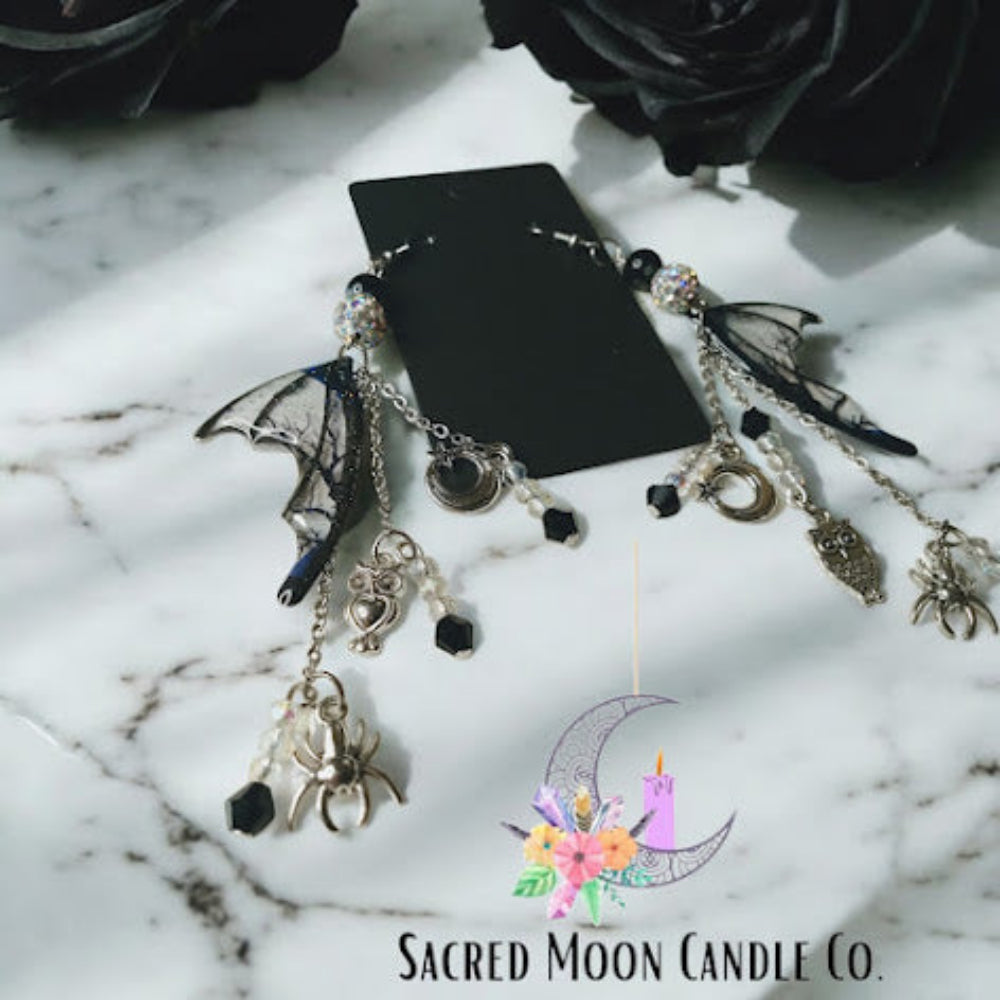 Sacred Moon Candle Co witches road batwing earrings with silver chains and spider charms on marble surface