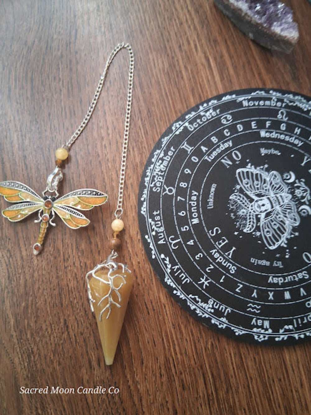 Golden healer quartz pendulum with dragonfly charm and black circular pendulum board from Sacred Moon Candle Co