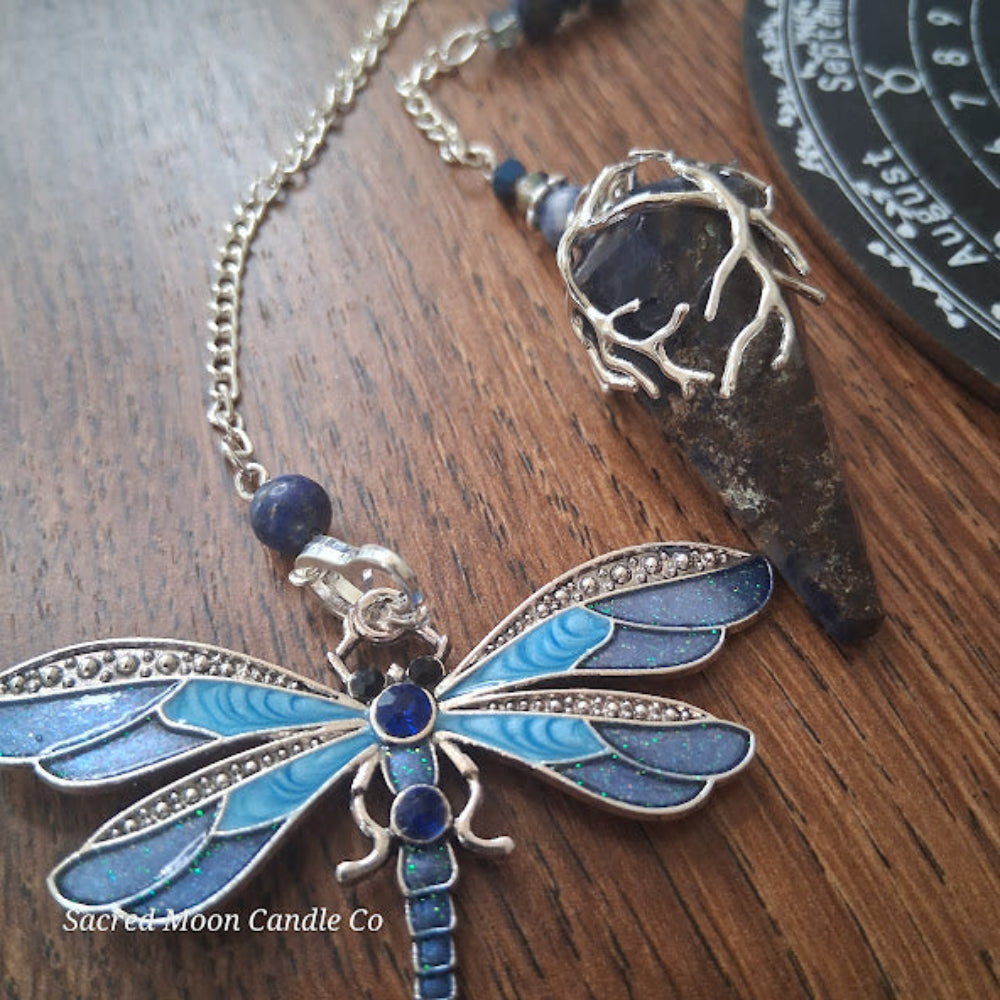 Sodalite and lapis lazuli pendulum with silver dragonfly charm on wooden surface from Sacred Moon Candle Co