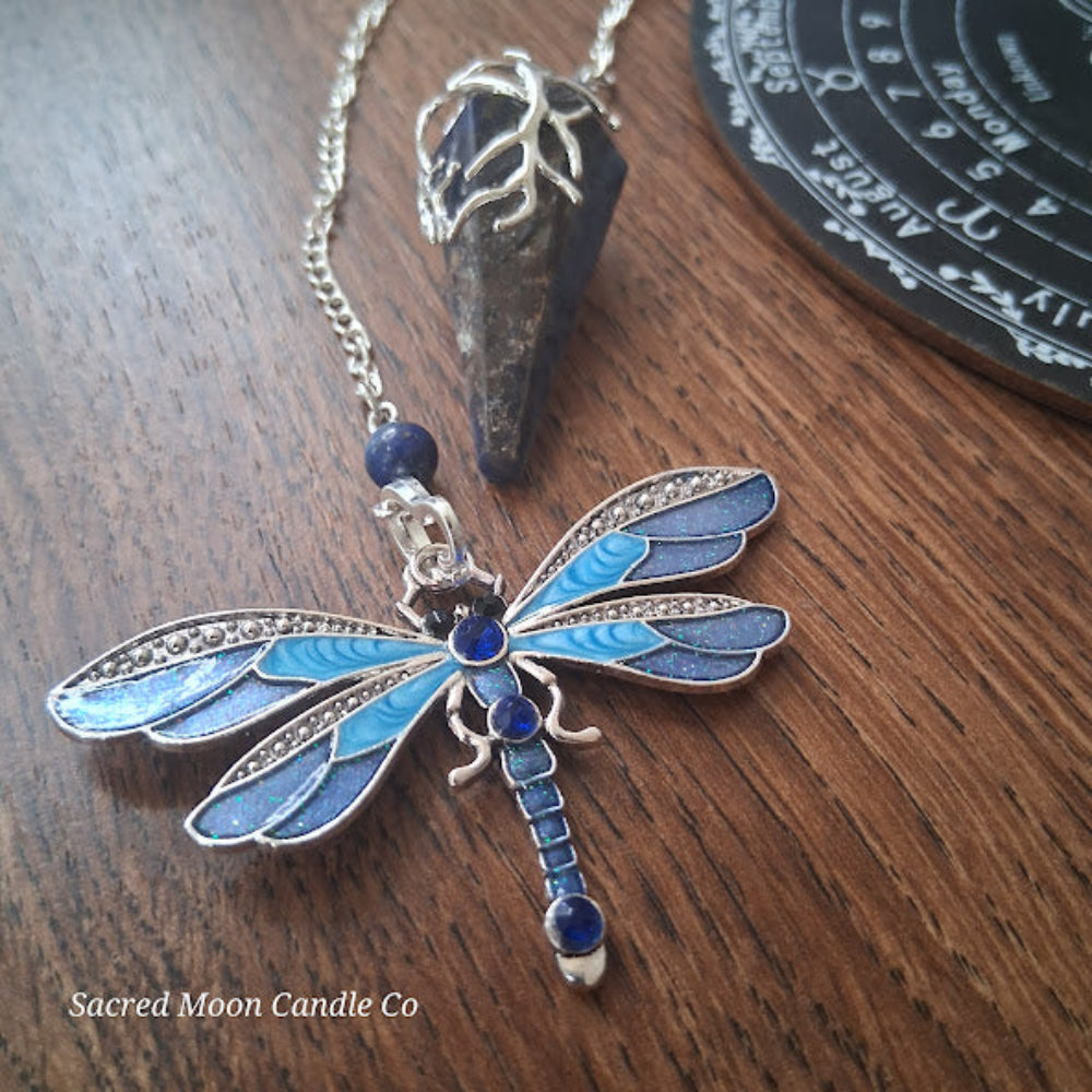 Sodalite and lapis lazuli pendulum with blue dragonfly charm on wooden surface by Sacred Moon Candle Co